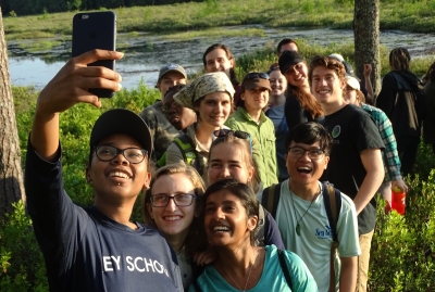 a large group of summer intern students smiles for a group selfie in Tom Swamp in summer