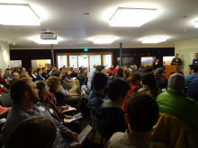 Audience view of a full room in the Fisher Museum at the 2018 Harvard Forest Symposium, with 3 speakers at a podium at front