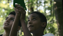 Two middle school students stand in a forest measuring the height of a tree