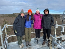Image shows the four Harvard Forest winter interns (2024) standing atop a research tower.