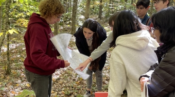 Image shows Harvard Forest Senior Ecologist Audrey Barker Plotkin, left, showing a map to several students in the forest. By Dave Orwig.