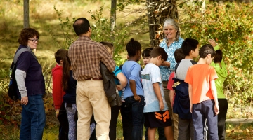 Image shows Pamela Snow, in teal/white shirt, giving a tour to students at Harvard Forest. 