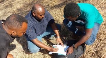 Image shows Ahmed Siddig, center, taking notes in the field