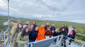 a group of Harvard community members smiles from the top of a tall metal tower in the woods