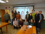 A dozen Harvard Forest winter interns and mentors smile in a conference room front of a screen 