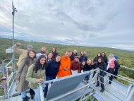 a group of Harvard community members smiles from the top of a tall metal tower in the woods