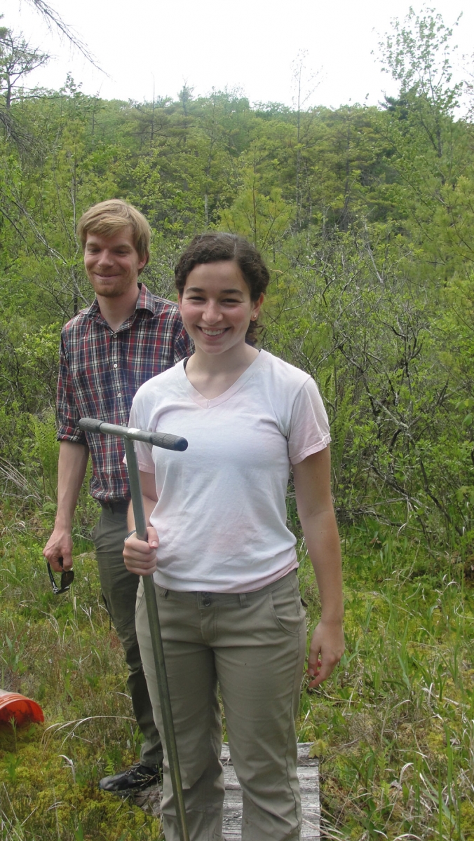 Megan Wilcots and Marco Keiluweit standing on a boardwalk in a wetland. Megan is holding a soil corer.