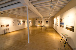 A large room that is an art gallery with artwork hanging on the walls