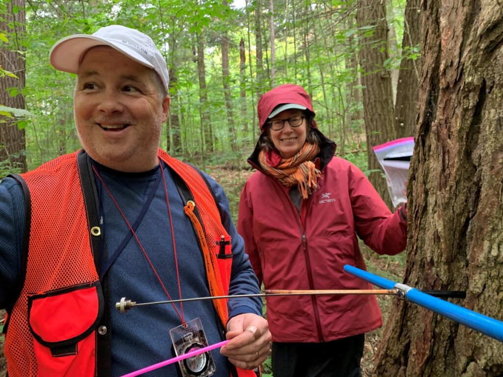 Two people standing next to a tree that has an increment borer embedded in it with a tree core protruding