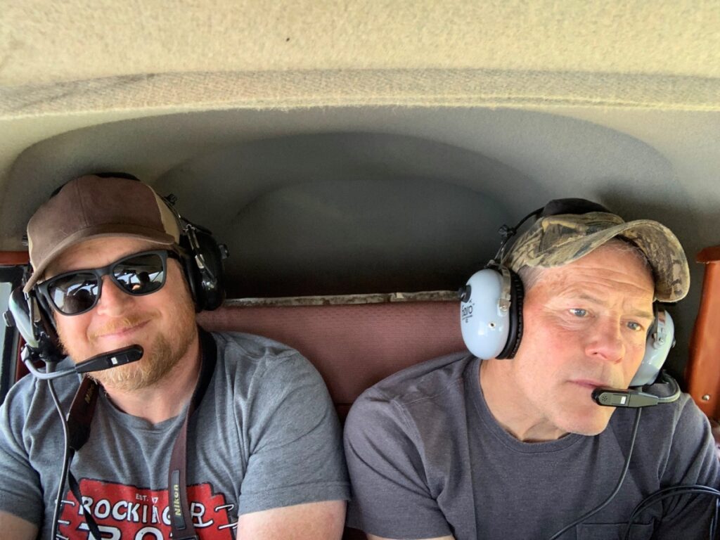 Two men wearing aviation headsets seated inside a small airplane