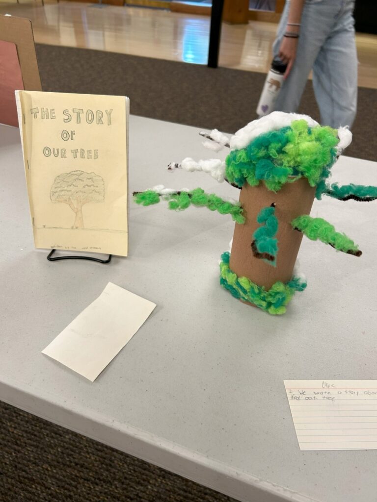 A tree crafted out of paper and pipe cleaners next to a handmade book entitled "The Story of Our Tree"