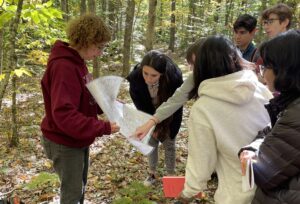 Image shows Harvard Forest Senior Ecologist Audrey Barker Plotkin, left, showing students data on a large piece of paper in the woods.