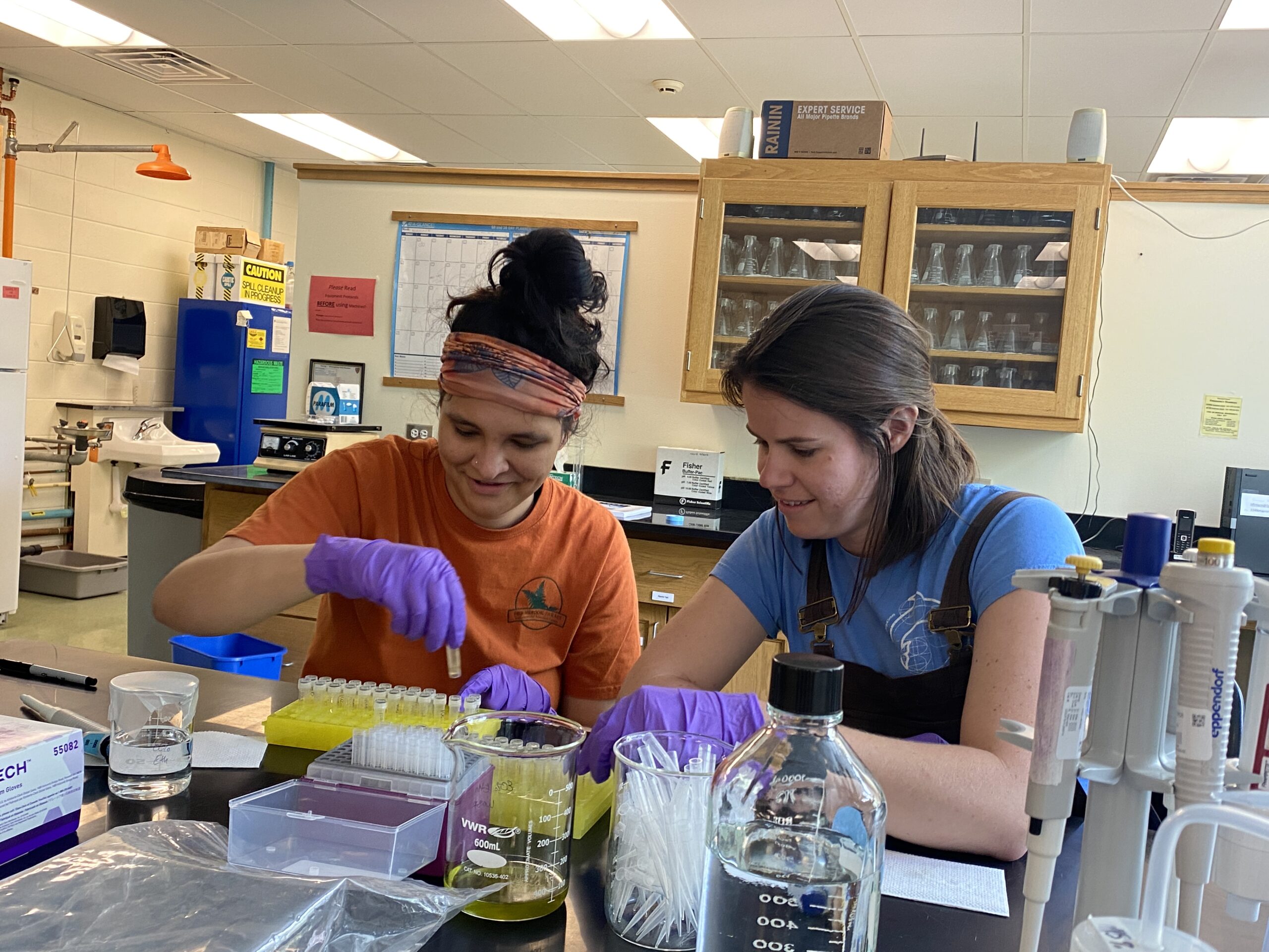 Image shows two females measuring out materials in an indoor lab.