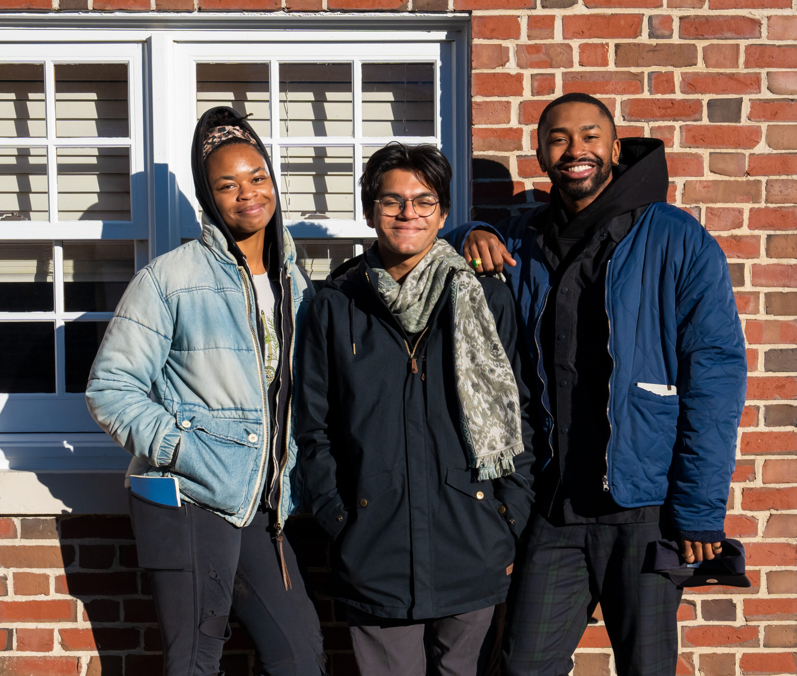 Kashish stands with Nia and Tyler, smiling, in front of the brick wall and window of the Harvard Forest archive